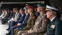 Mehrere Soldaten und Zivilisten aus verschiedenen Ländern sitzen unter einem Zelt nebeneinander.