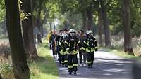 Feuerwehrmänner- und frauen marschieren auf einer Allee und haben Atemschutzmasken auf.