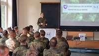 Viele Soldaten sitzen in einem Hörsaal und schauen auf eine Leinwand und eine vortragende Soldatin