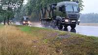 Ein Militär-LKW fährt auf einer Landstraße, ihm folgen weitere militärische Fahrzeuge.