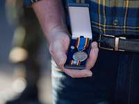 Nicht bei allen wurde die Medaille an der Kleidung angebracht Nahaufnahme der Hand eines Zivilisten, die eine Schatulle mit Medaille, Bandschnalle und Anstecknadel hält