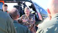 Im Vordergrund sieht man Personen von hinten, die auf einen erklärenden Oberstarzt blicken, der vor einem Hubschrauber steht.