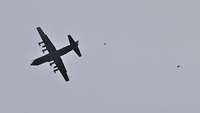 Fallschirmspringer springen aus einem Flugzeug am blauen Himmel, der Schirm ist noch geschlossen.