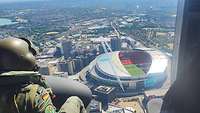 Blick über die Schulter des Bordmechanikers aus dem Hubschrauber heraus auf das Oval eines Stadions