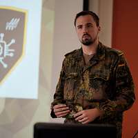 Ein Soldat steht vor einer Videowand und hält eine Karte in der Hand.