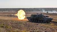 Ein Panzer schießt auf einem Übungsgelände, ein großer Feuerball entsteht.