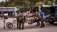 Vor Sanitätszelten werden Verletzte von Soldaten jeweils auf einer Trage aus Fahrzeugen entladen.