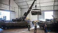 Austausch der Verschleißteile Ein Bergepanzer hebt mit seinem Kran einen Motor an