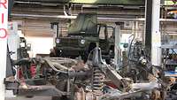 Ein zerlegter Fahrzeugrahmen mit Rostansatz im Vordergrund, dahinter eine Bühne mit Geländewagen aufgebockt.