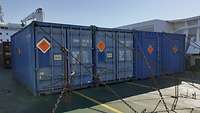 Container stehen auf einem Schiffsdeck und sind mit Ketten verzurrt. Damit sind sie vor Verrutschen geschützt.