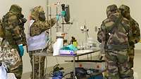 Four persons clad in olive protective clothing standing in a laboratory