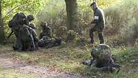 Mehrere Soldaten helfen einem auf dem Boden liegenden verletzten Kameraden. Ein Soldat sichert sie liegend.
