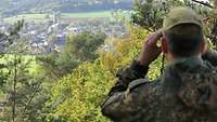 Ein Soldat beobachtet mit einem Fernglas in Richtung einer Ortschaft.