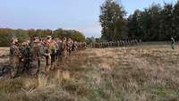 Soldatinnen und Soldaten stehen in Formation auf einer Wiese. Der General steht in der Mitte vor seiner Übungstruppe.