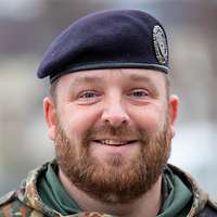 Porträt eines lächelnden Soldaten mit Bart und dunkelblauem Barett