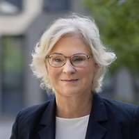 Ein Porträt von Ministerin Lambrecht, die lächelnd in einem sonnigen Innenhof steht.