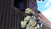 Auf einer Leiter stehend, schießt ein Soldat mit seinem Gewehr durch ein Fenster. 