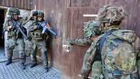 Vier Soldaten stehen an einer Scheunentür aus Holz. Zwei rechts, zwei links. 