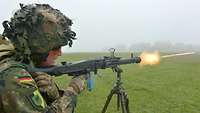 Ein Soldat schießt mit einem Maschinengewehr auf einem Dreibein auf ein Ziel. Mündungsfeuer entsteht