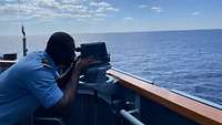 Ein Soldat schaut in ein Gerät in der Nock eines Schiffes.