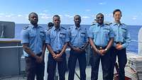 Fünf Marinesoldaten stehen an Deck eines Schiffes und schauen in die Kamera.