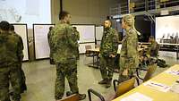 Eine Soldatin und zwei Soldaten stehen im Gespräch in einer Halle beisammen.