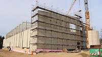 Rohbau Hallenschießanlage Gera Ein großer Kran, an dem ein Richtkranz hängt, steht vor einem gewaltigen Beton-Rohbau auf einer Baustelle