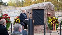 Ministerin Lambrecht spricht am Rednerpult vor einem Gedenkstein mit einer verhüllten Tafel.