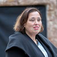 Eine Frau spricht am Rednerpult vor einem Gedenkstein mit einer verhüllten Gedenktafel.