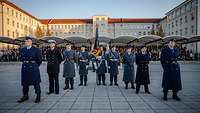 Soldaten stehen mit der Truppenfahne auf einem Platz vor einer Tribüne mit Zuschauern