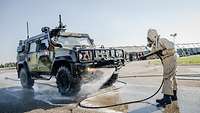 Ein Soldat in einem Schutzanzug besprüht ein Militärfahrzeug mit Dekontaminationsmittel