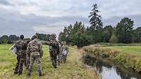 Eine Gruppe Soldaten steht an einem kleinen Fluss und begutachtet die Umgebung.