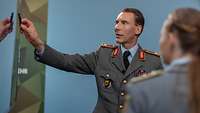 Brigadegeneral Freuding steht einer Soldatin gegenüber und zeigt mit dem Stift auf einen Bildschirm.
