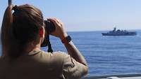 Eine deutsche Soldatin beobachtet mit einem Fernglas ein vorbeifahrendes Schiff
