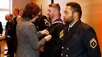 Eine Frau befestigt eine Medaille an der ,,1.Geige" (Dienstanzug der Marine) an einem Marinesoldat