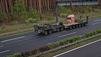 Ein LKW der Bundeswehr fährt auf einer Autobahn. Er transportiert einen Findling auf dem eine deutsche Flagge gebunden ist.
