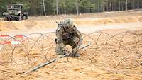 Ein Soldat schiebt ein Sprengrohr unter eine S-Draht Rolle