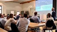 Teilnehmer im Hörsaal mit Blick auf die Leinwand