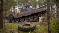 Ein Panzer klettert über einen Graben. Davor liegt ein Reifen mit Moos.