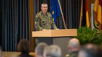 Ein Soldat steht am Rednerpult und spricht zum Plenum