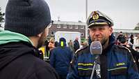 Ein Marineoffizier in blauer Arbeitsjacke und mit weißer Schirmmütze.
