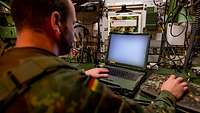 Ein Soldat sitzt in einer Kabine an einem Laptop.