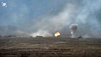 Inmitten einer kargen Landschaft zwischen drei Panzern in ihren Stellungen entsteht eine Detonation mit Feuer und Rauch.