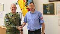 Ein Oberstleutnant der Bundeswehr schüttelt die Hand eines Feuerwehrmannes in einem Büro in einer Kaserne.