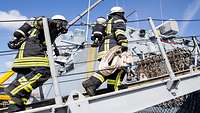Two Bundeswehr firefighters wearing respiratory protection go aboard a ship.