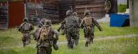 Soldat im Feuer Mehrere Soldaten laufen mit Waffen in der Hand über eine Wiese auf ein Haus zu,