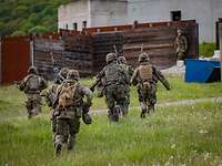Soldat im Feuer Mehrere Soldaten laufen mit Waffen in der Hand über eine Wiese auf ein Haus zu,