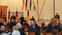 Viele Menschen sitzen in einem Gebäude.