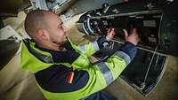 Einbau des Datenspeichers Eine Person befindet sich an der Technik des "RecceLite-Pods" und hält in den Händen einen Datenspeicher.