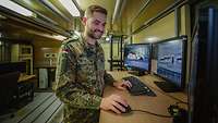 Ein Soldat schaut auf einen von drei Computerbildschirmen. Nebenbei bedient er die Tastatur sowie die Computermaus..